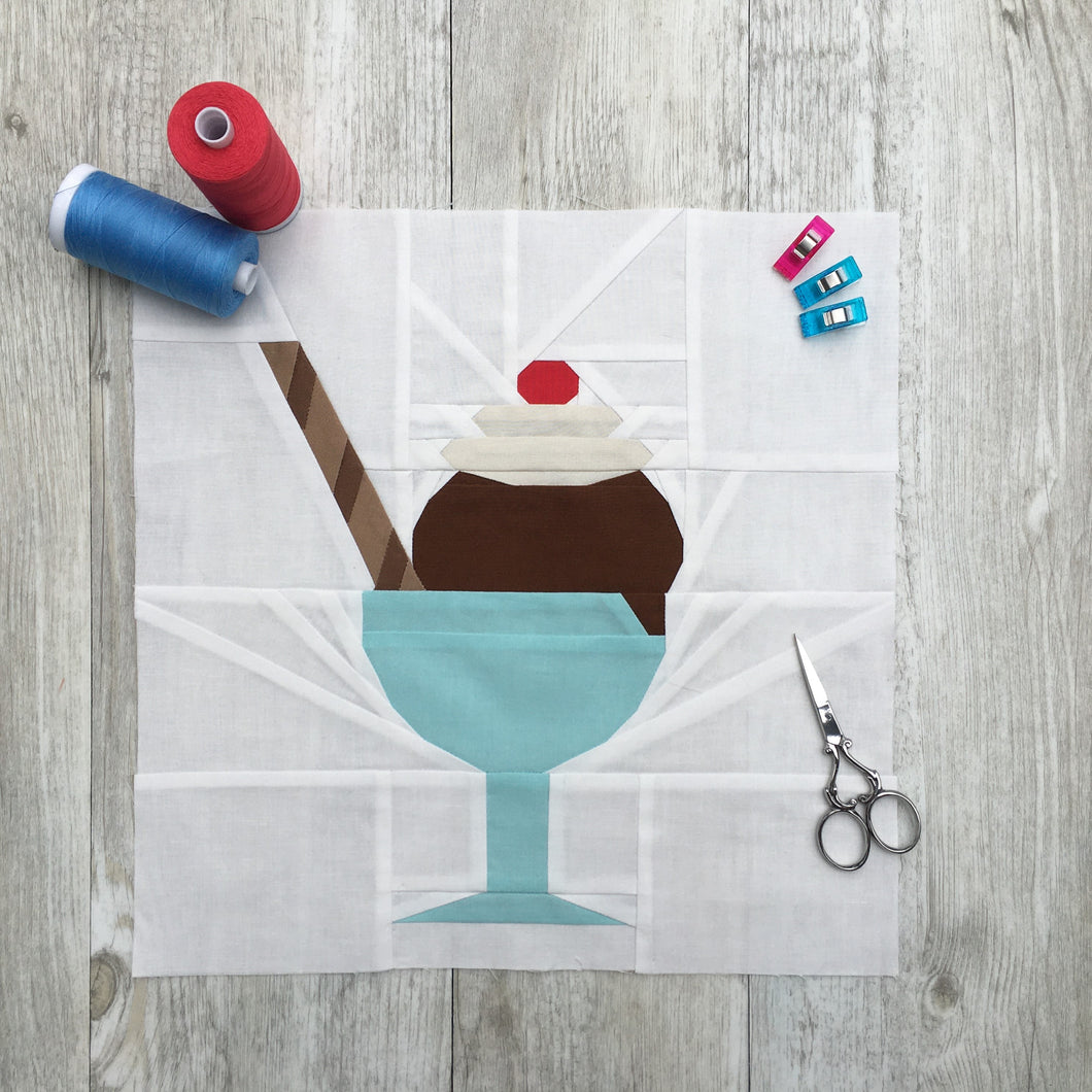 Ice Cream Bowl quilt block pattern by Penny Spool Quilts. Part of the Ice Cream Sunday collection. Sample shows chocolate ice cream topped with whipped cream and a red cherry, and a striped chocolate wafer straw, in a turquoise bowl with stem, on white background. Shown with spools of thread, pins and small scissors